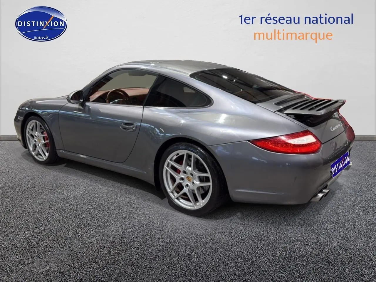 Vue 3/4 arrière droite d'une Porsche 911 (997) Carrera PDK gris métallisé avec jantes alu et aileron déployé.