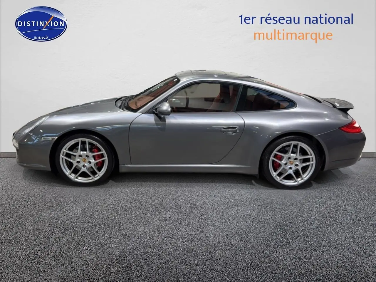 Profil côté gauche d'une Porsche 911 (997) Carrera PDK gris métallisé avec jantes alu et aileron arrière déployé.