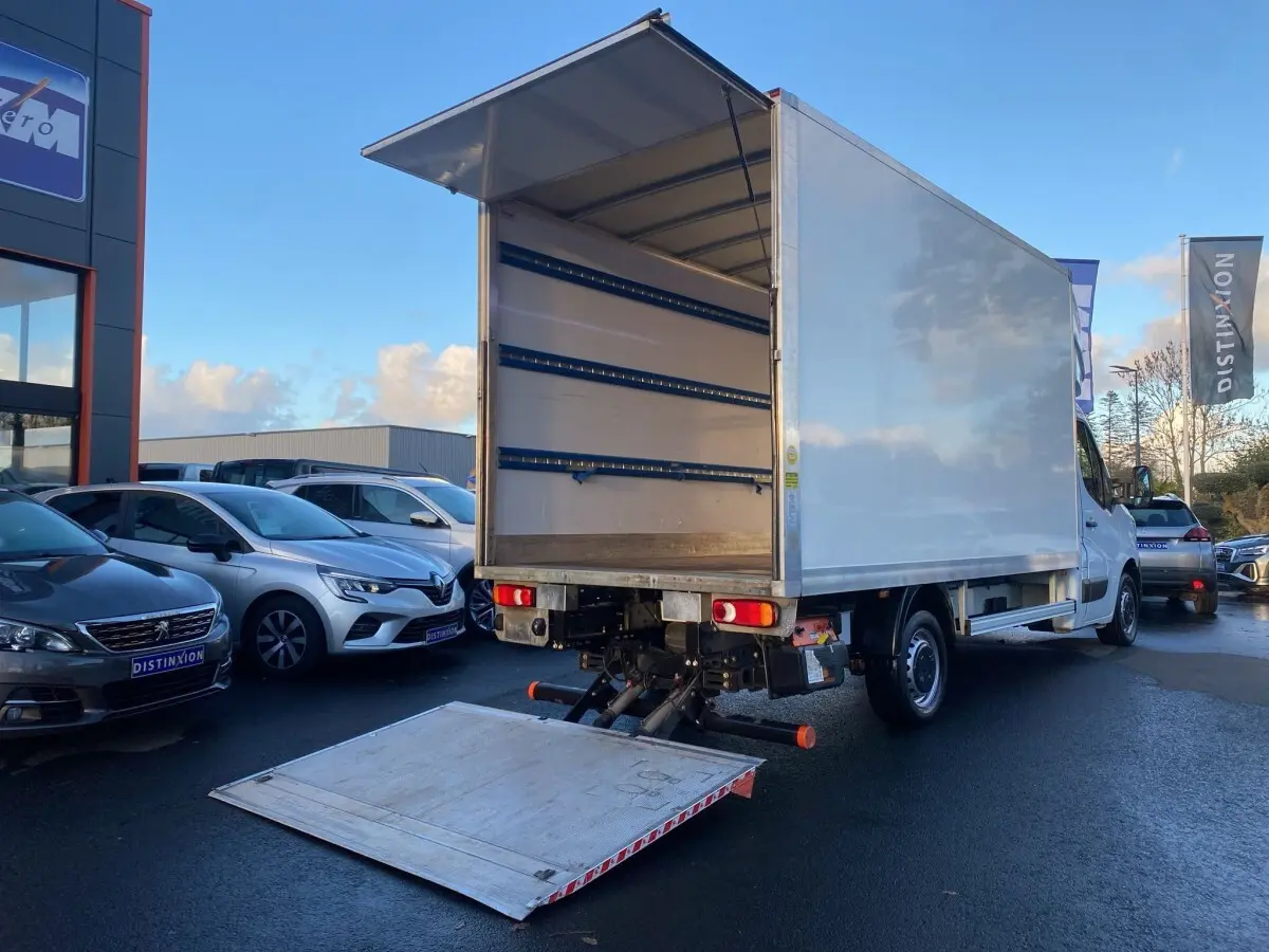 Vue 3/4 arrière d’un Renault Master blanc avec hayon élévateur déployé, montrant l’espace de chargement vide.