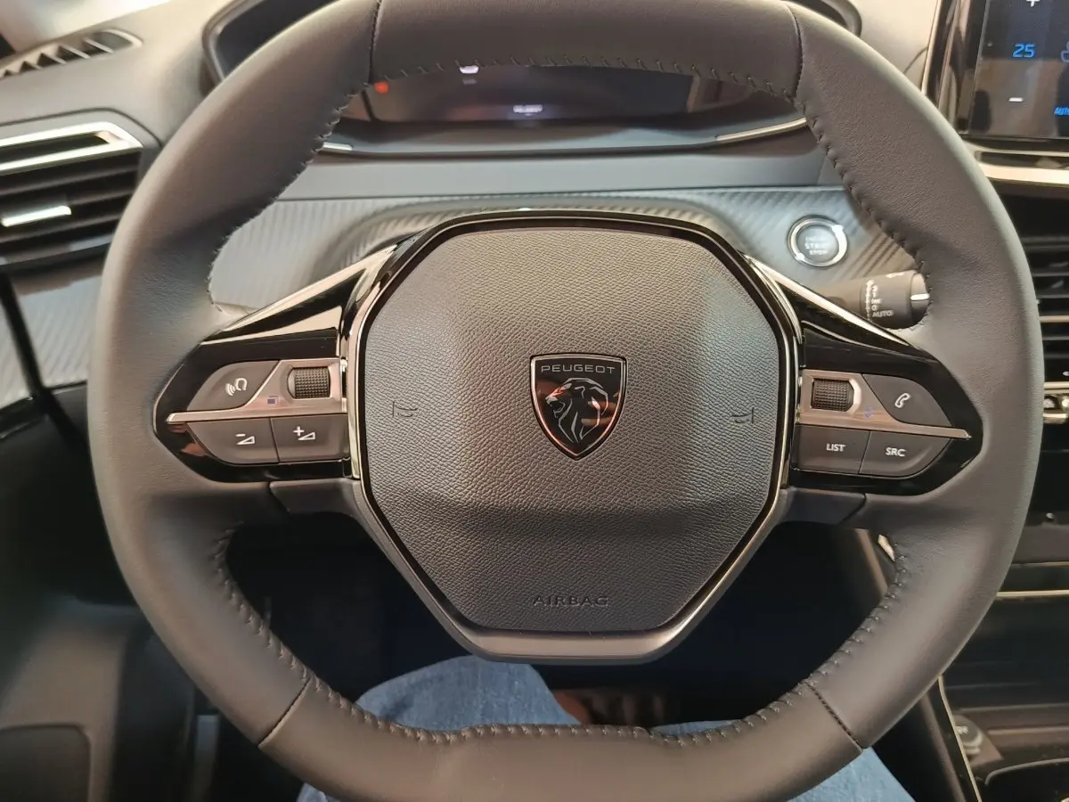 Volant cuir noir de Peugeot 208 électrique 2024 vu de face, avec commandes intégrées et bouton démarrage visible.