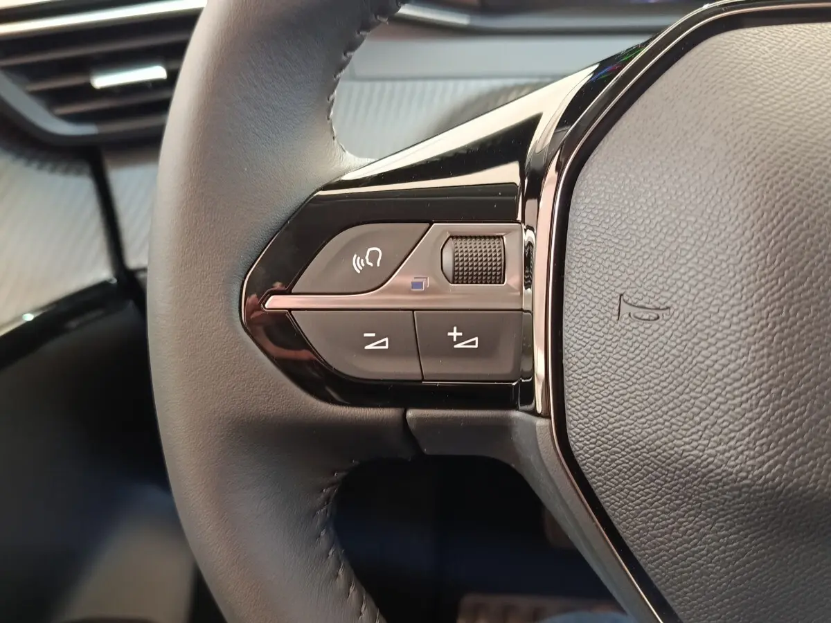 Gros plan sur les commandes gauche du volant cuir noir du Peugeot 208 électrique blanc 2024, avec boutons multifonctions.