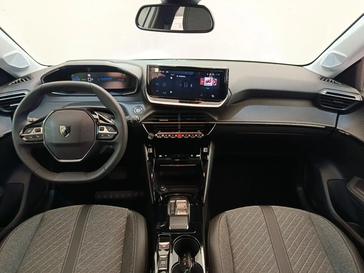 Vue intérieure avant de la Peugeot 208 électrique 2024, tableau de bord noir avec écran tactile central et volant compact cuir.
