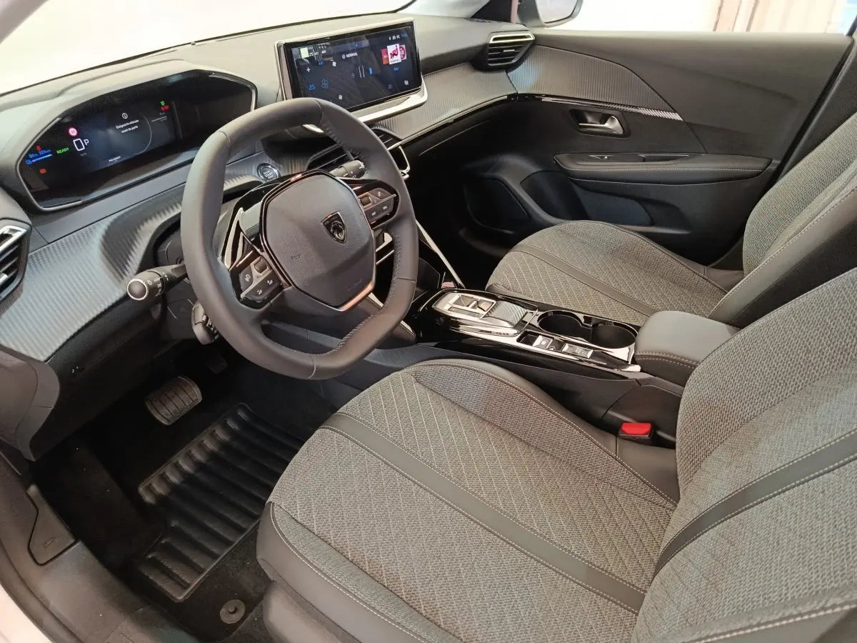 Vue intérieure côté conducteur de la Peugeot 208 électrique 2024, sièges gris et tableau de bord avec écran tactile.