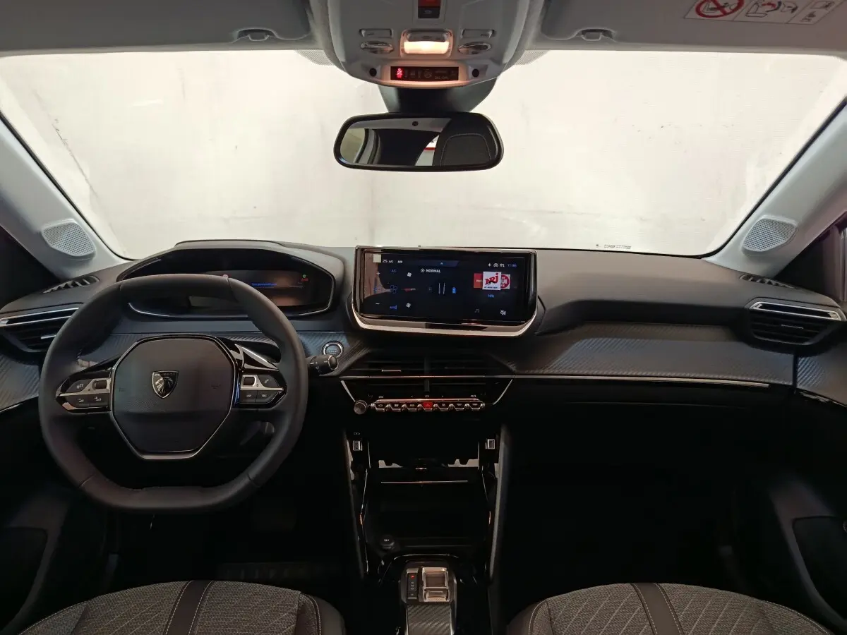Vue intérieure frontale du tableau de bord et volant cuir noir de la Peugeot 208 électrique 2024, avec écran tactile central.