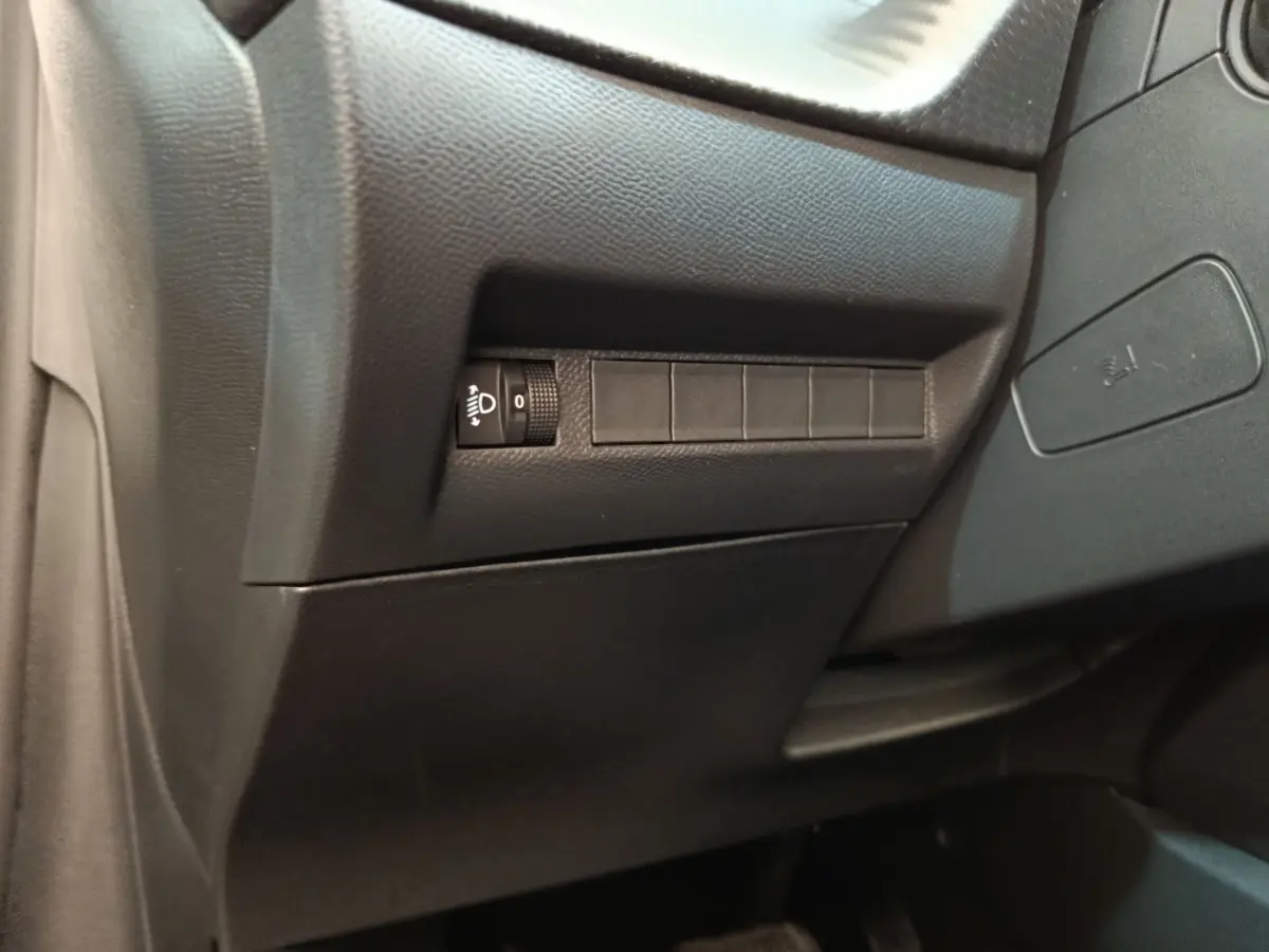 Détail intérieur côté conducteur du tableau de bord noir avec commande réglage hauteur phares Peugeot 208 électrique 2024.