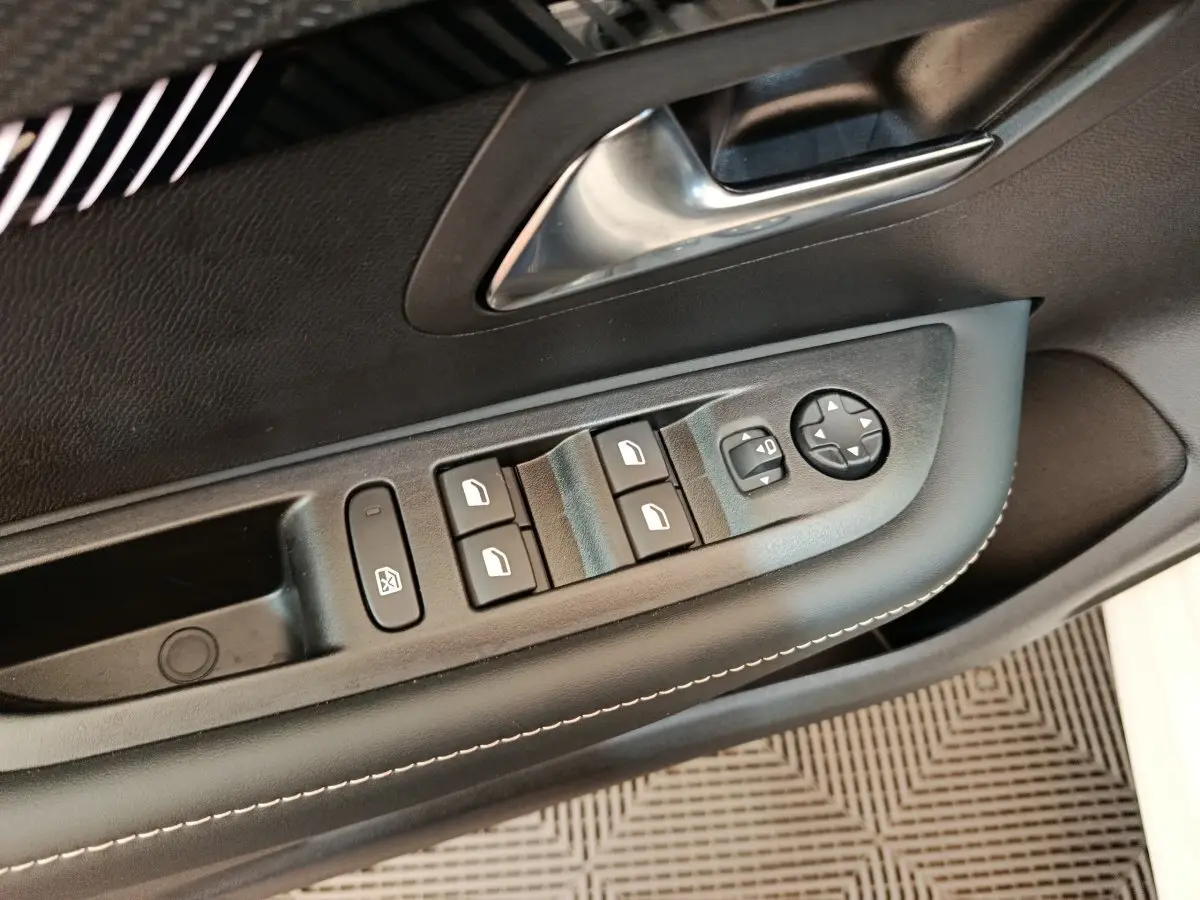 Gros plan sur la commande des vitres électriques et rétroviseurs côté conducteur d'une Peugeot 208 blanche de 2024.