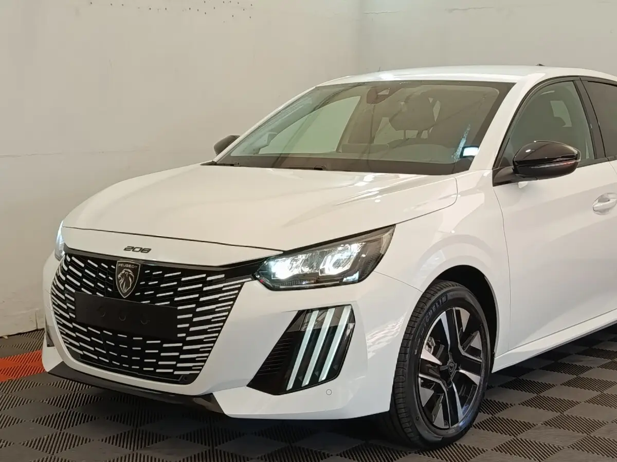 Peugeot 208 électrique blanche vue 3/4 avant droit, avec phares LED allumés et calandre distinctive noire.