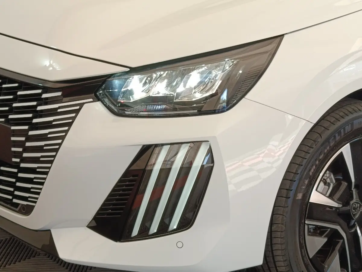 Gros plan sur l'avant droit blanc du Peugeot 208 électrique 2024, mettant en valeur les phares LED et la calandre distinctive.