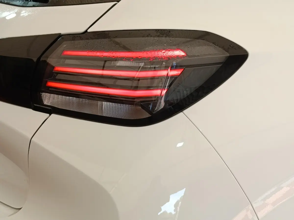Gros plan sur le feu arrière droit allumé d’une Peugeot 208 électrique blanche, soulignant son design moderne.