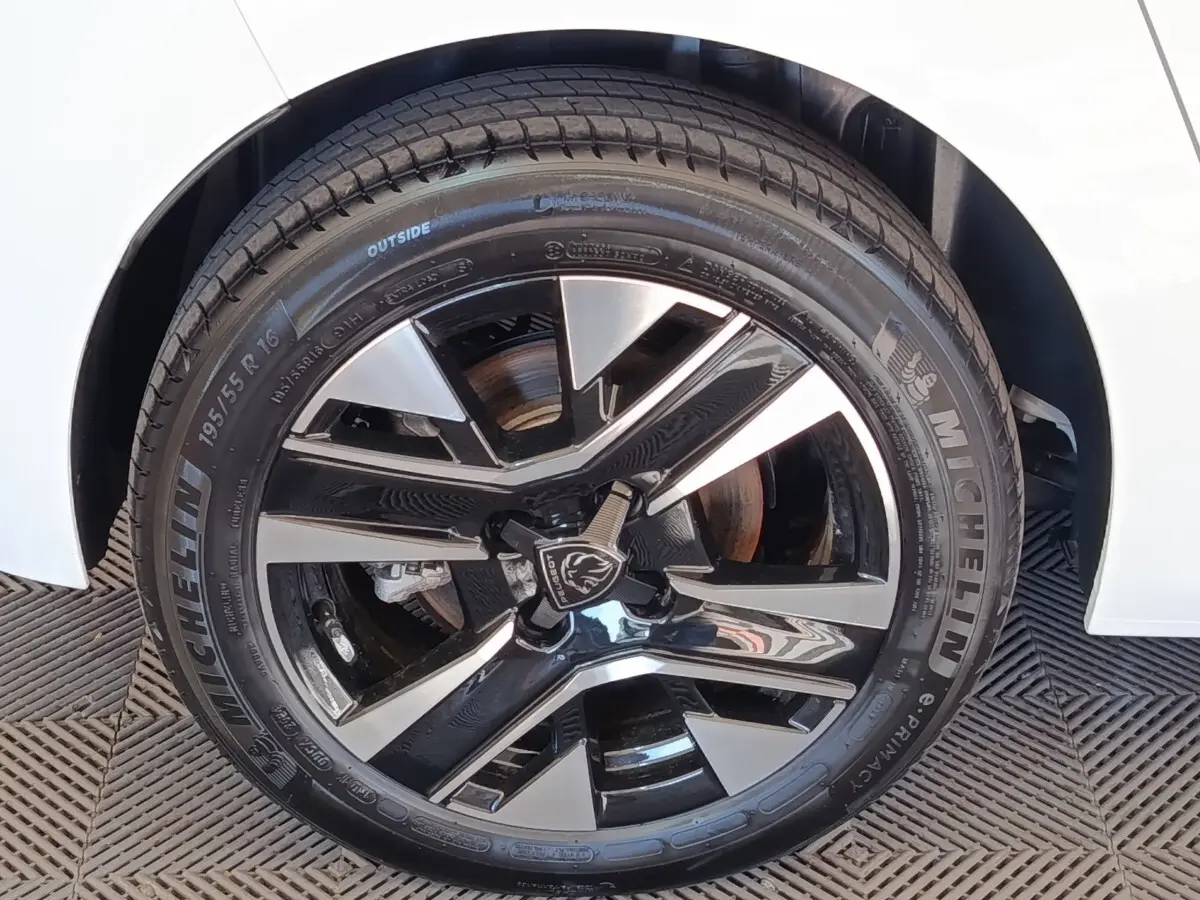 Gros plan sur la roue avant droite d’une Peugeot 208 électrique blanche, jante alliage noir et argent.