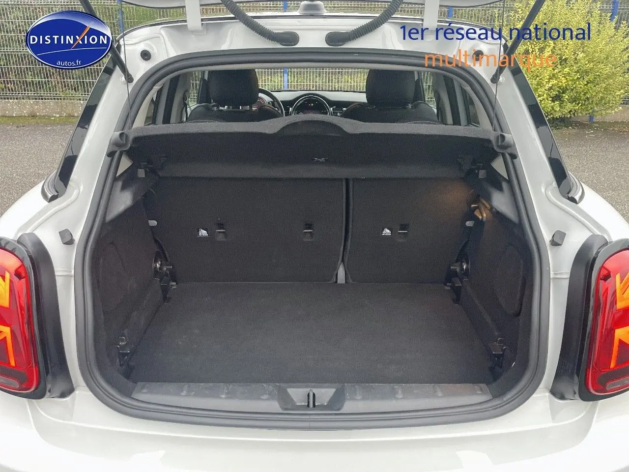 Coffre ouvert vu de l'arrière d'une MINI 1.5 136CH blanc nacré, montrant l'espace de chargement et la banquette arrière.