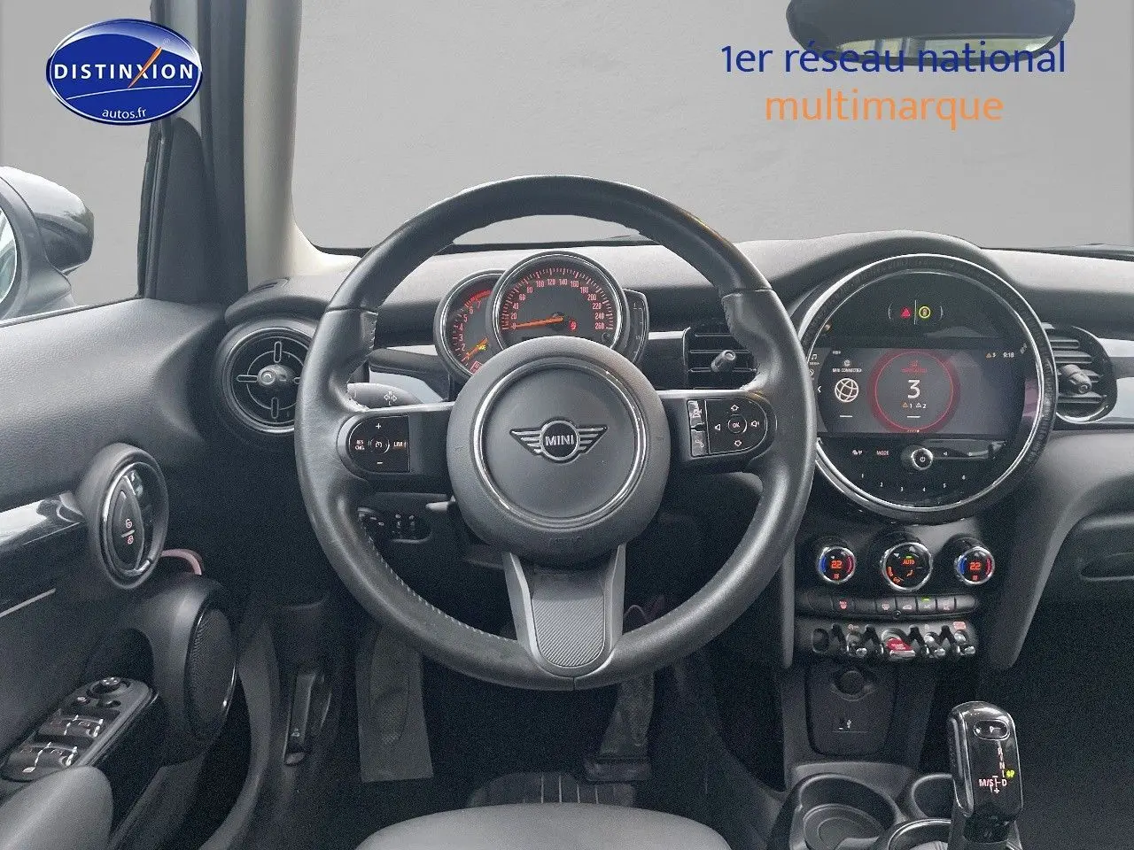 Vue intérieure centrée sur le volant et le tableau de bord d'une MINI blanche nacrée 2023 avec écran numérique et commandes modernes.