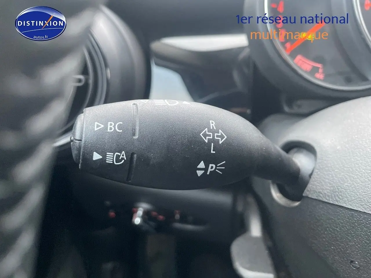 Gros plan sur la commande de clignotants à gauche du volant d'une MINI blanche nacrée 2023, avec marquages blancs visibles.