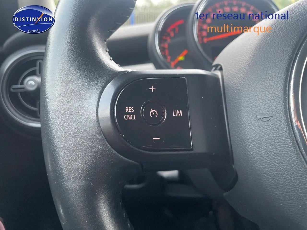 Gros plan sur le volant noir de la MINI 1.5 136CH STEPTRONIC 2023, avec commandes de régulateur de vitesse visibles.