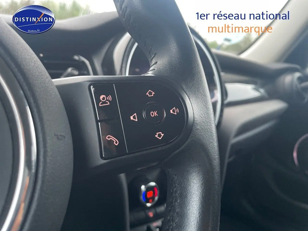 Gros plan sur les commandes du volant noir d'une MINI 1.5 136CH 2023, intérieur moderne avec tableau de bord en arrière-plan.