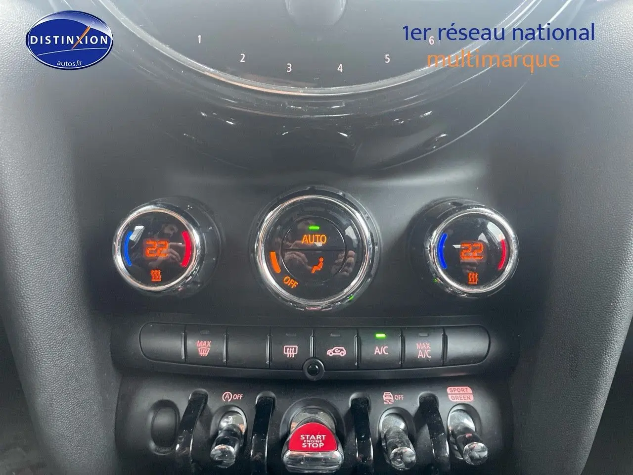 Gros plan sur la console centrale de la MINI blanche nacrée 2023, montrant les commandes de climatisation et le bouton start/stop rouge.