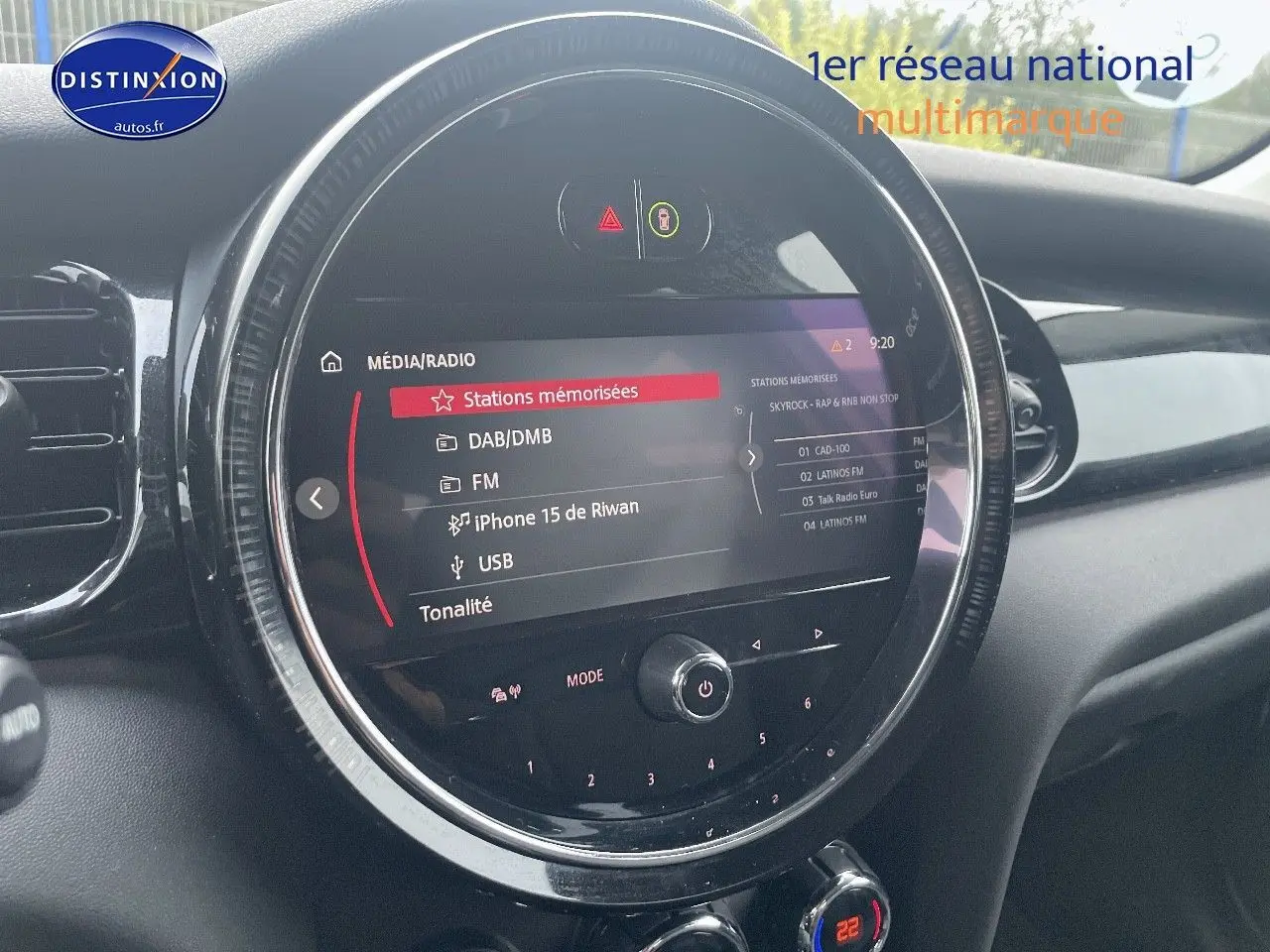 Gros plan sur l'écran central rond du tableau de bord d'une MINI blanche nacrée, affichant le menu média et radio.