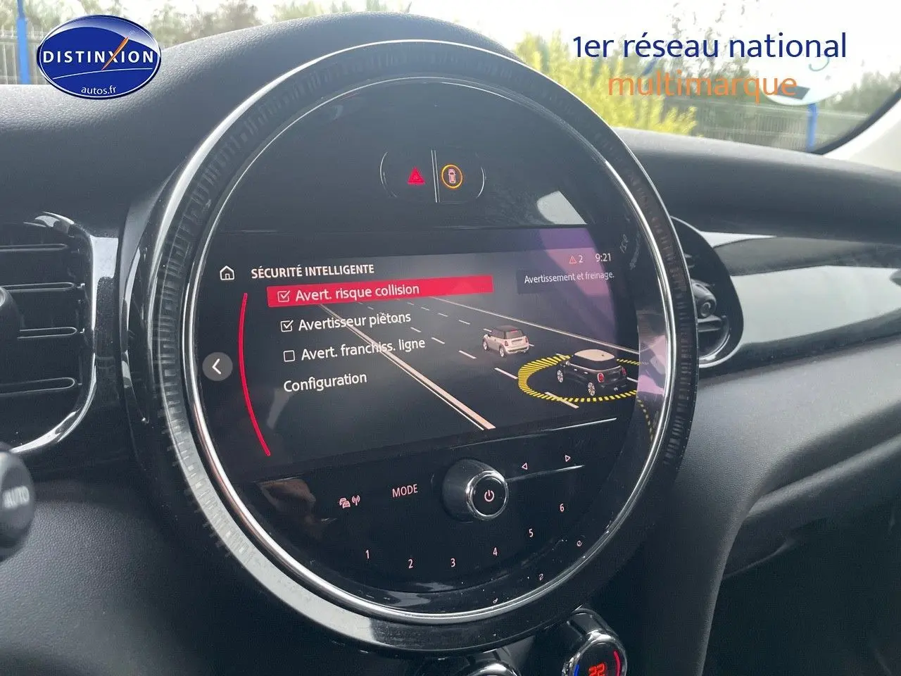 Vue rapprochée du tableau de bord de la MINI blanche nacrée 2023 montrant l'écran central avec alertes de sécurité active.