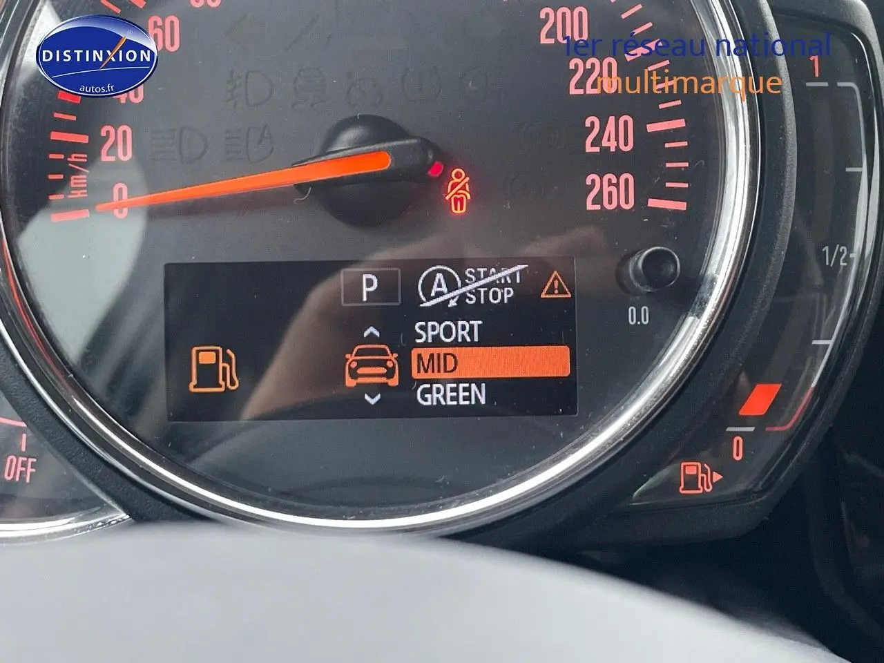 Gros plan sur le tableau de bord digital d'une MINI blanche nacrée 2023, affichant le mode de conduite et jauge d'essence.