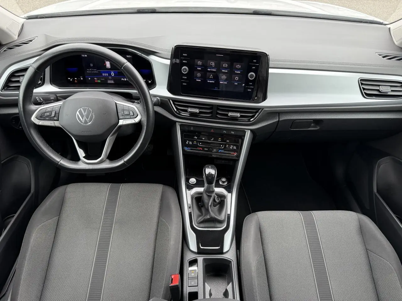 Vue intérieure frontale du tableau de bord et volant du Volkswagen T-Roc 2022 avec écran tactile central et sièges gris.
