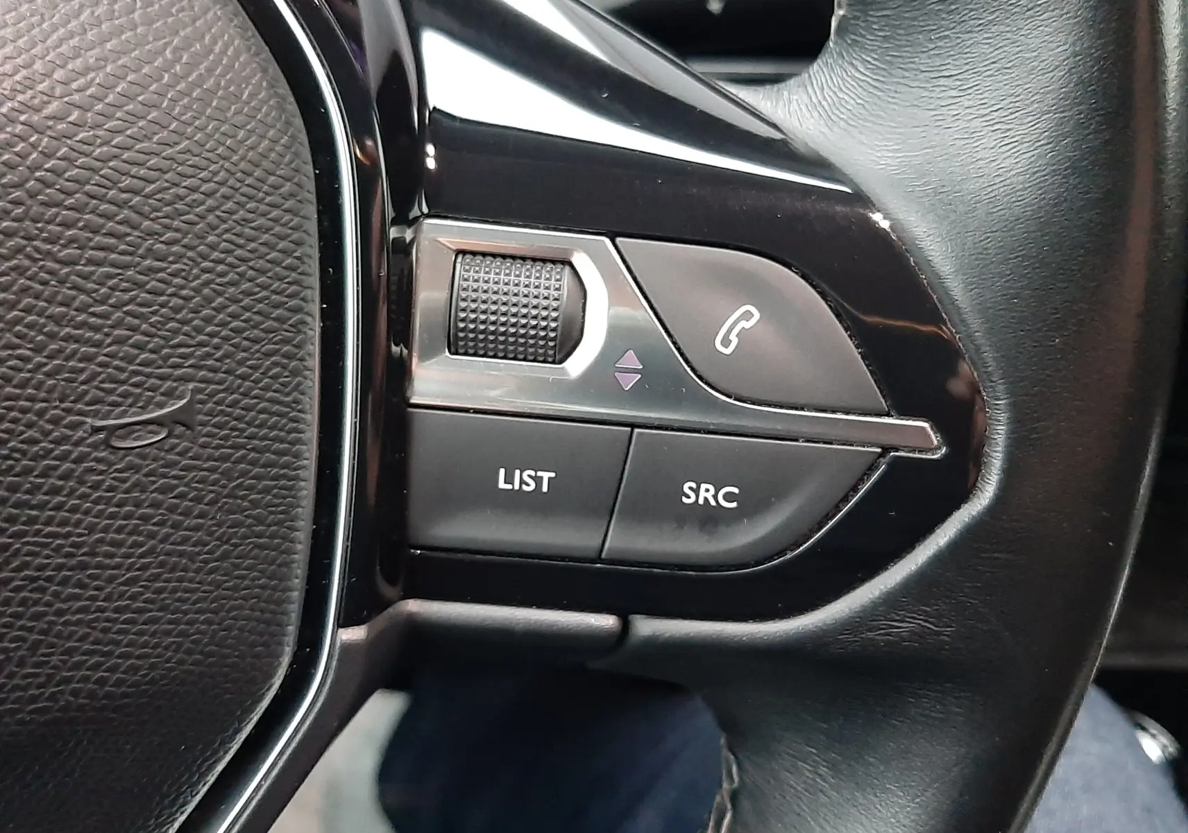 Gros plan sur les commandes gauche du volant noir du Peugeot 508 blanc, avec boutons LIST, SRC et téléphone.