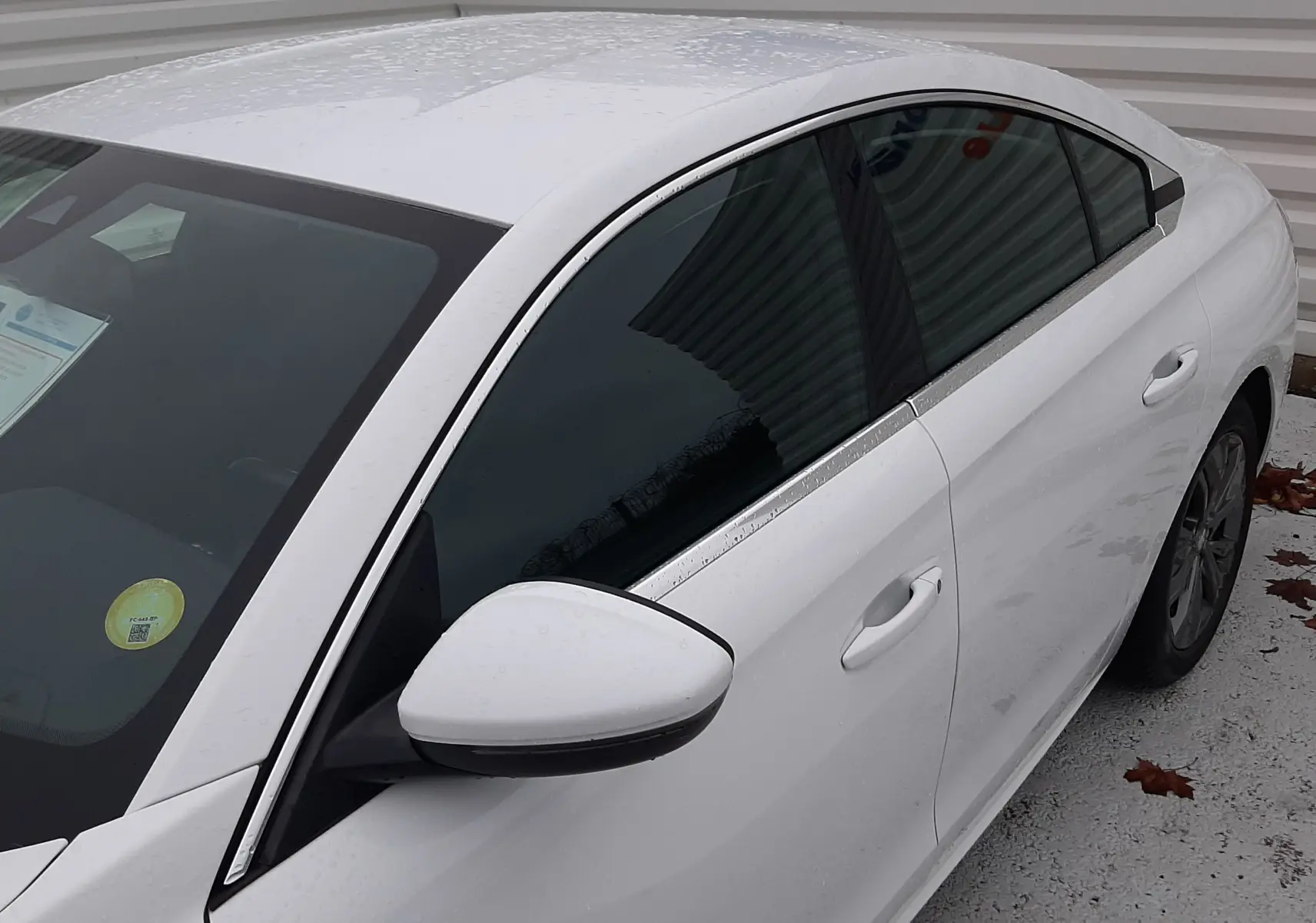 Vue 3/4 avant droit d'une Peugeot 508 blanche avec vitres teintées et rétroviseur blanc, stationnée près d'un mur métallique.