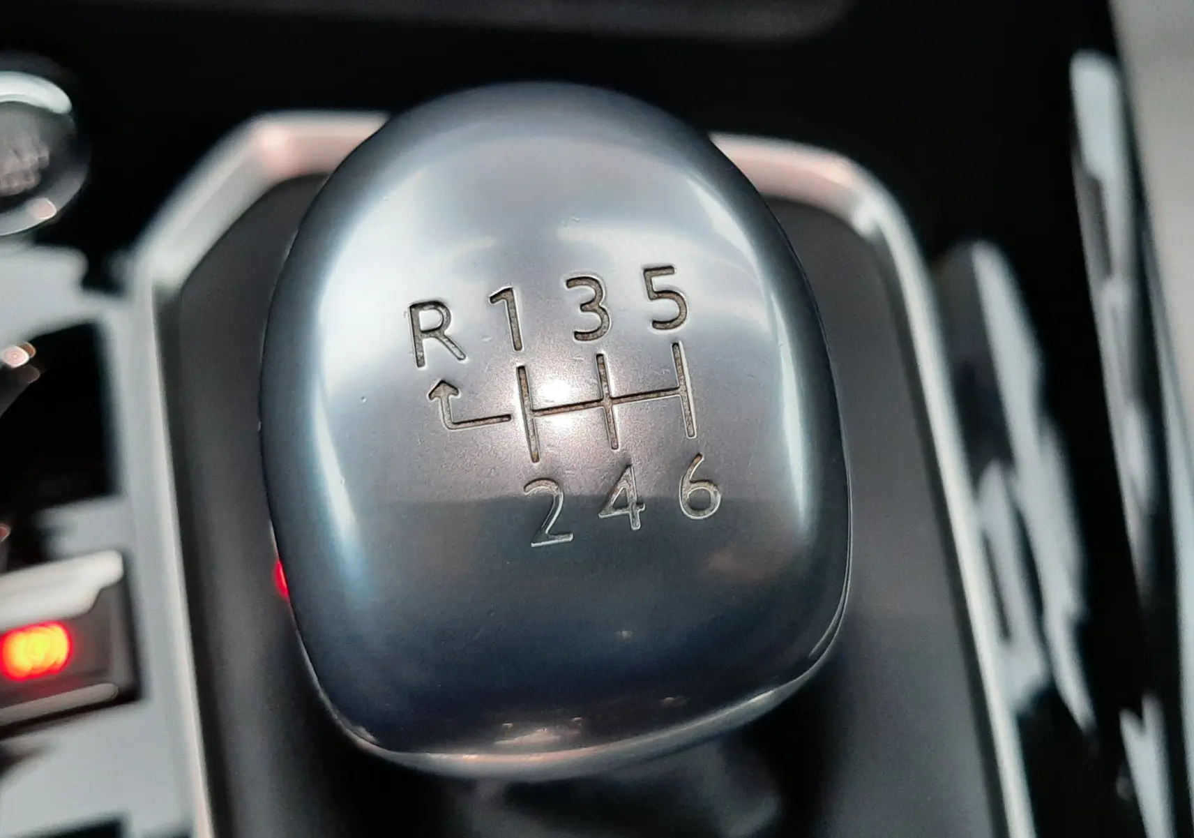 Gros plan sur le levier de vitesses manuel gris métallique de la Peugeot 508 blanche, montrant la grille à 6 rapports et la marche arrière.