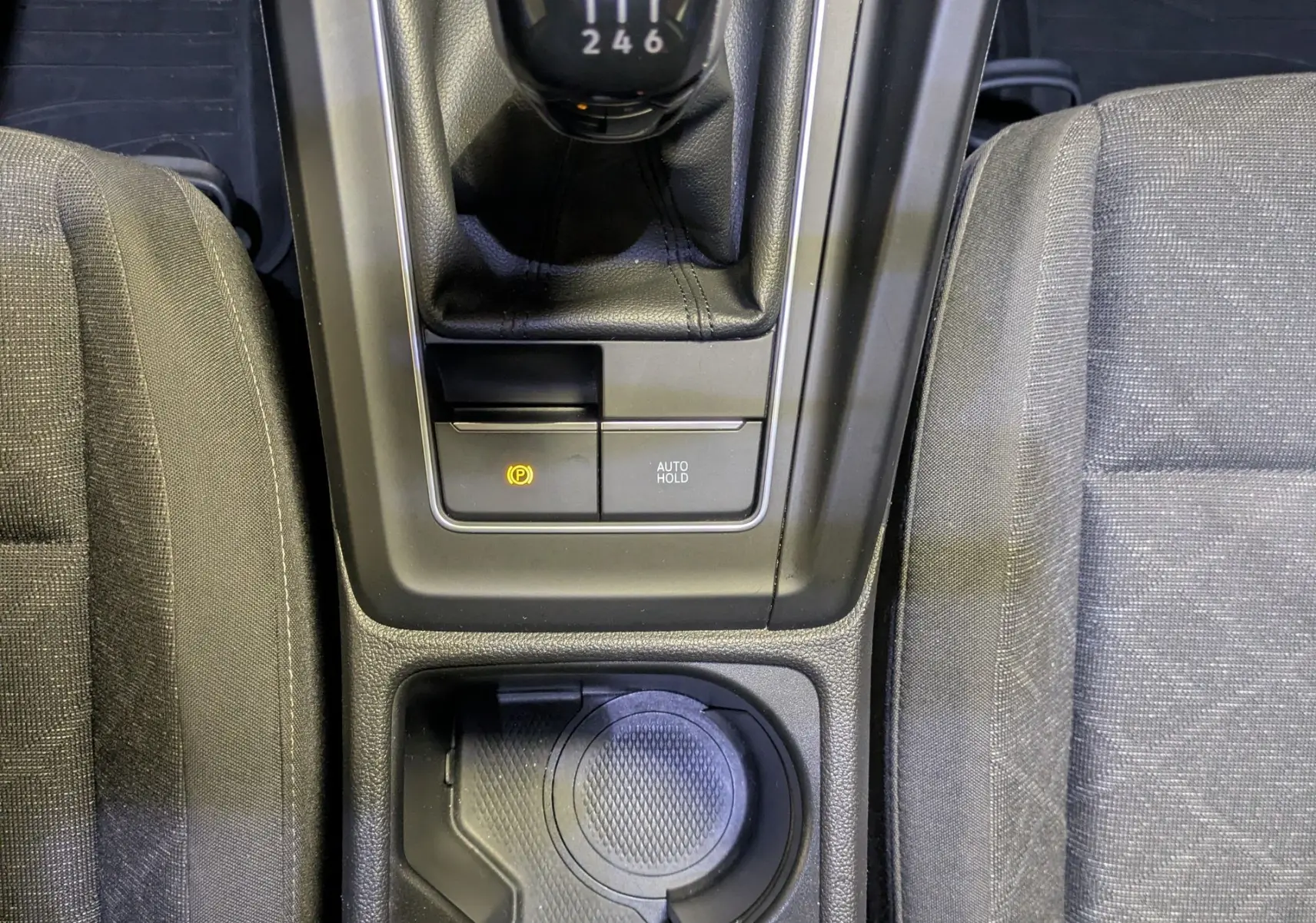 Vue plongeante sur la console centrale noire d'une Volkswagen Golf 2024, avec levier de vitesse manuel et porte-gobelets.