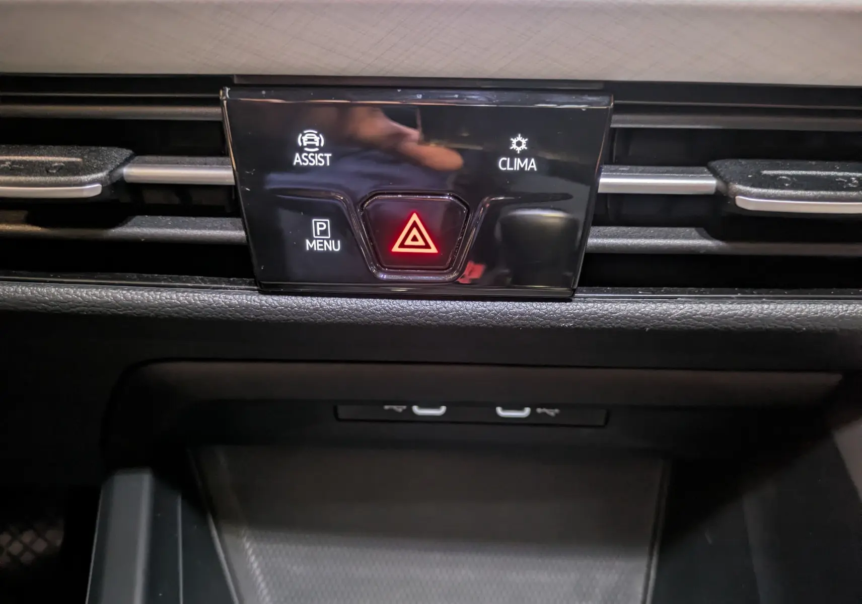 Détail du tableau de bord de la Volkswagen Golf 2024 noir, bouton d'alerte rouge et commandes d'assistance et climatisation.