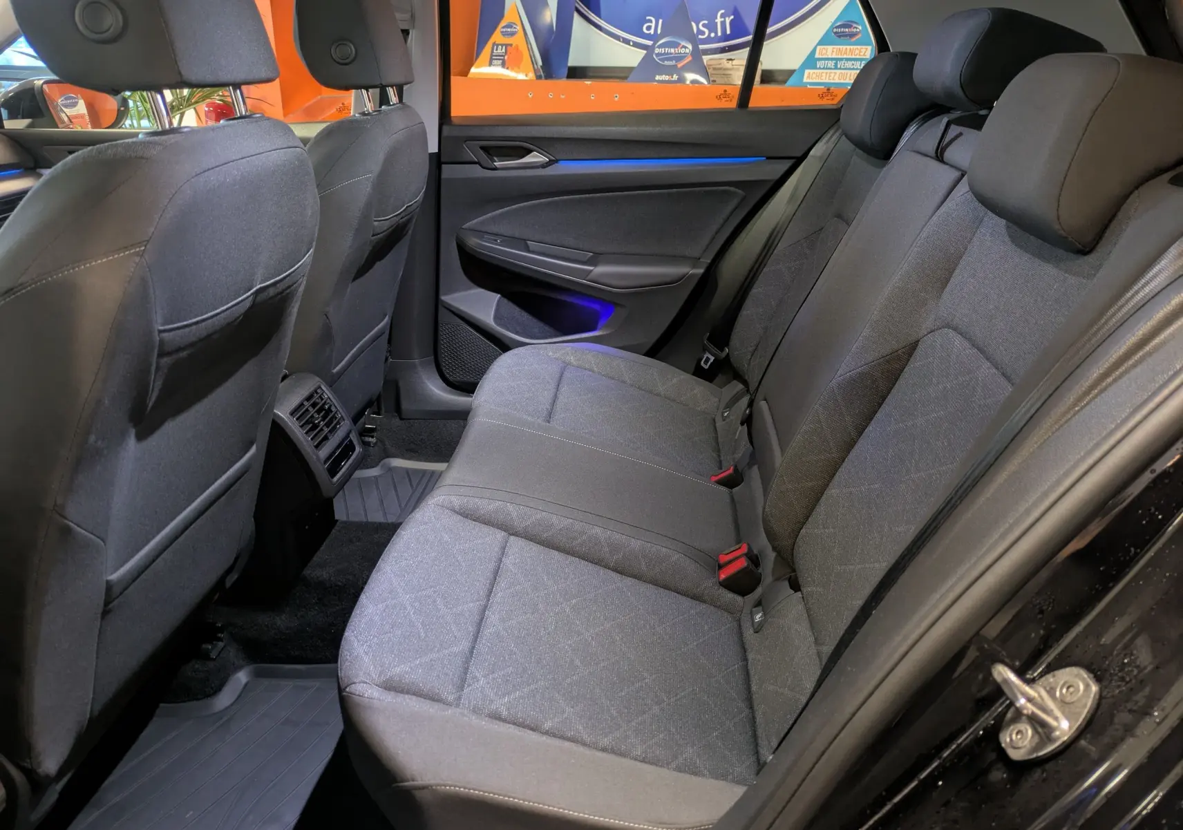 Vue intérieure côté droit des sièges arrière gris d'une Volkswagen Golf 1.5 eTSI Style 2024 avec éclairage d'ambiance bleu.