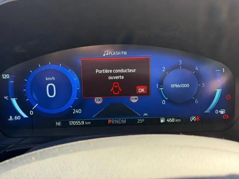 Tableau de bord numérique du Ford Kuga 1.5 EcoBlue 2023 affichant une alerte "Portière conducteur ouverte" en bleu et rouge.