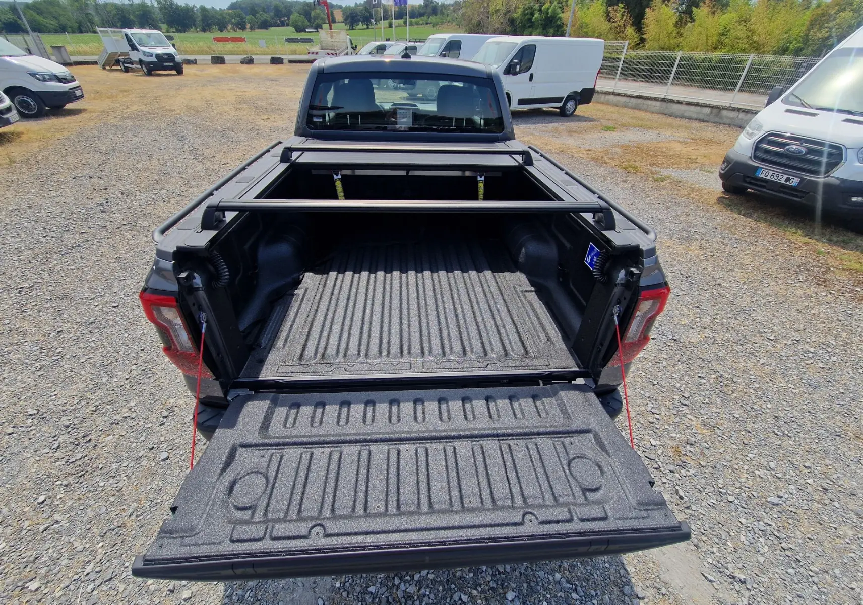Vue arrière du Ford Ranger Super Cabine gris carbone avec plateau ouvert, rideau rigide coulissant et barres de protection visibles.