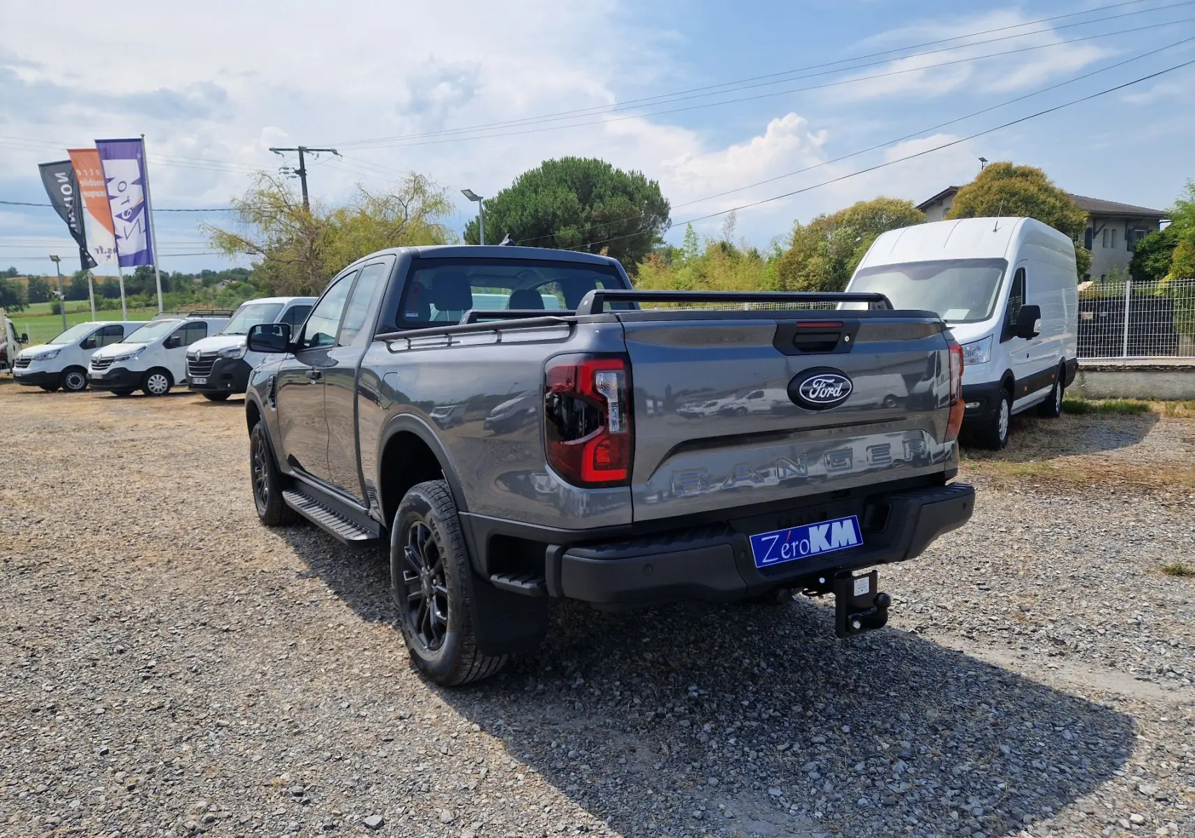 Ford Ranger Super Cabine gris carbone vu en 3/4 arrière droit, avec rideau de plateau rigide et barres de toit noires.