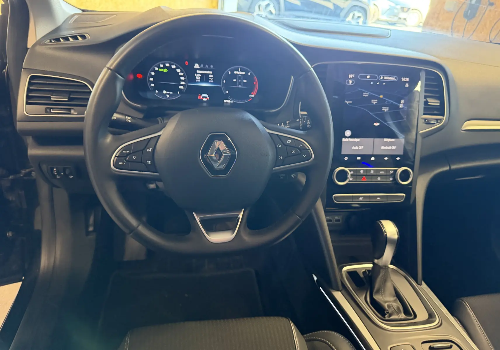 Vue intérieure de face du poste de conduite de la Renault Mégane Estate 2024 avec volant multifonction et écran tactile central.