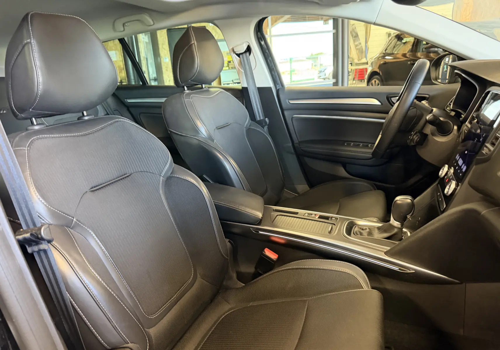 Vue intérieure côté conducteur de la Renault Mégane Estate 2024 avec sièges noirs et console centrale moderne.