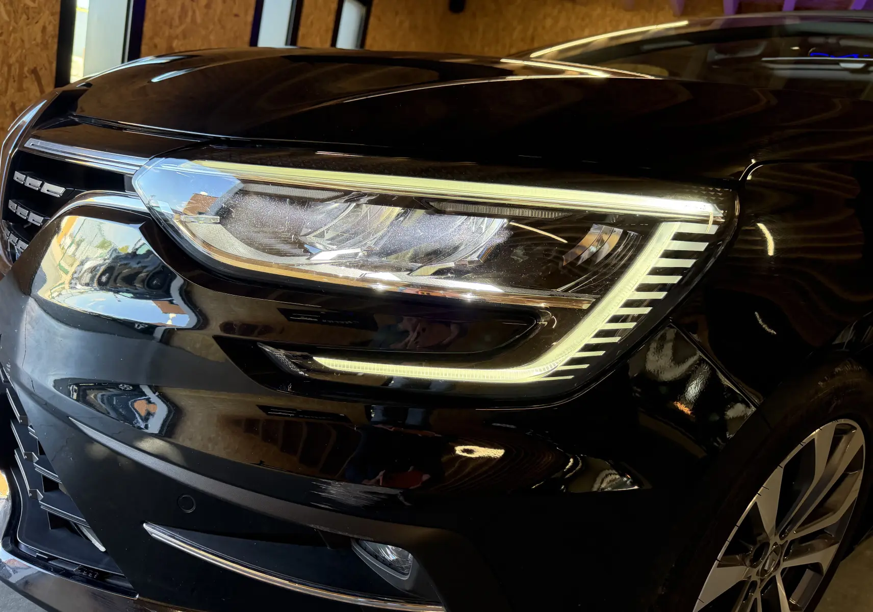 Gros plan sur le phare avant droit d'une Renault Mégane Estate noire 2024 avec peinture noir étoilé et jante visible.