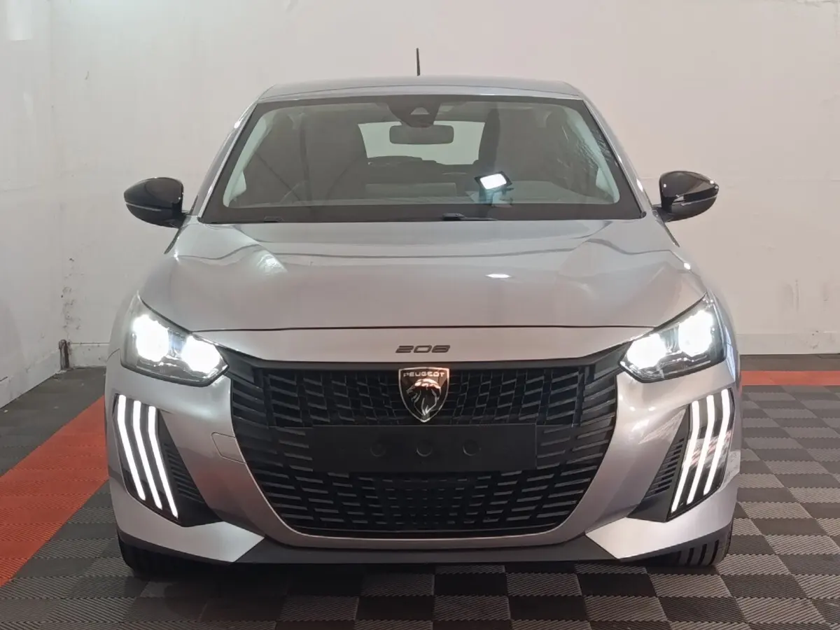 Peugeot 208 électrique gris clair vue de face avec phares LED allumés et signature lumineuse verticale distinctive.