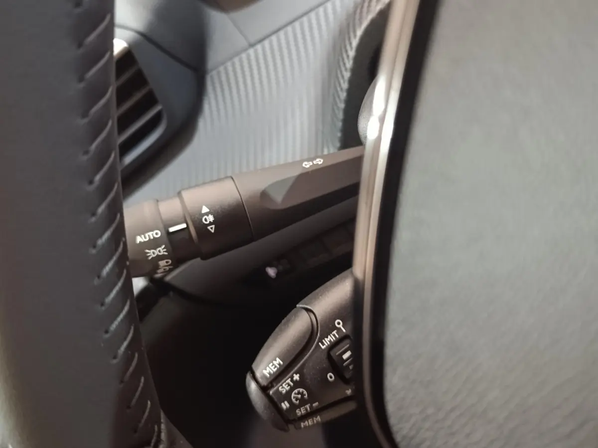 Gros plan sur le volant cuir noir de la Peugeot 208 électrique 2024, avec commandes de régulateur et éclairage.