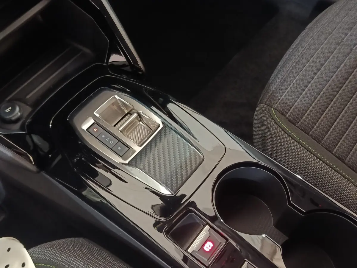 Gros plan sur la console centrale noire brillante de la Peugeot 208 électrique 2024 avec frein à main électrique et porte-gobelets.