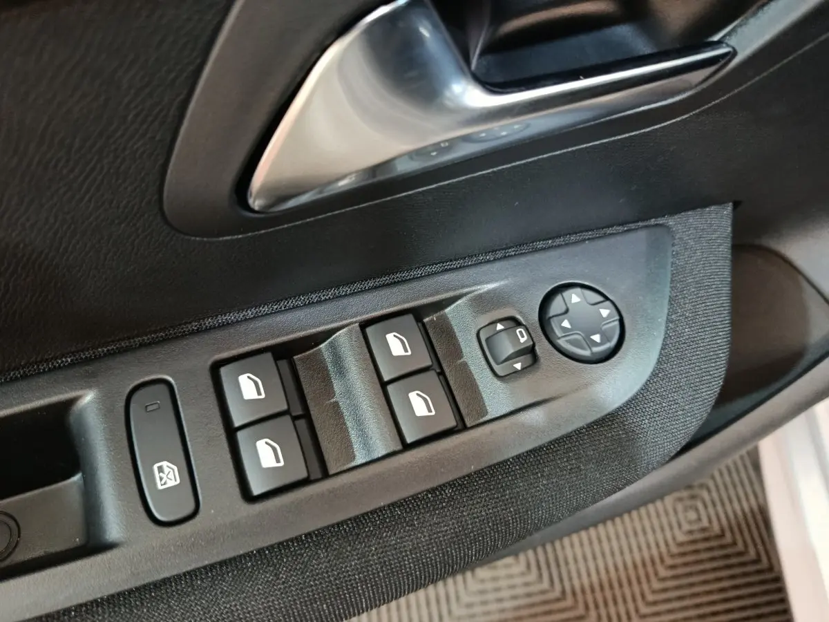 Gros plan sur les commandes de lève-vitres et rétroviseurs côté conducteur d’une Peugeot 208 électrique gris clair.