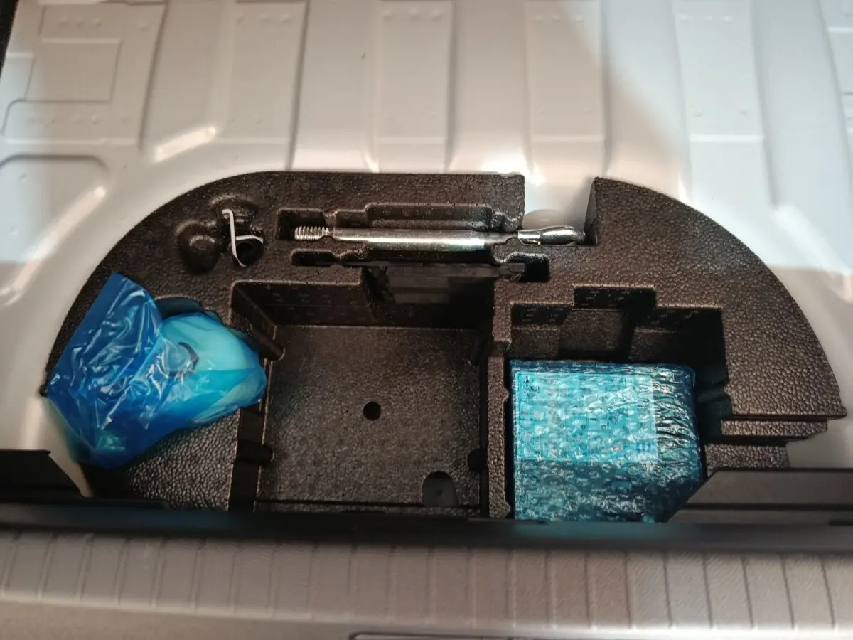 Rangement sous coffre de Peugeot 208 électrique 2024, compartiments en mousse noire avec outils et accessoires emballés.
