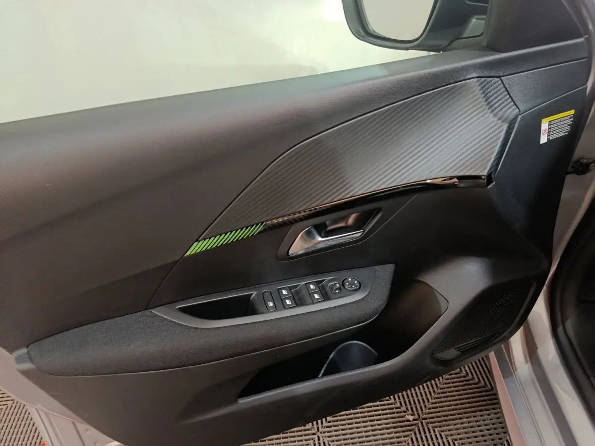 Vue intérieure côté gauche de la porte avant d’une Peugeot 208 électrique gris clair avec insert décoratif et commandes vitres.