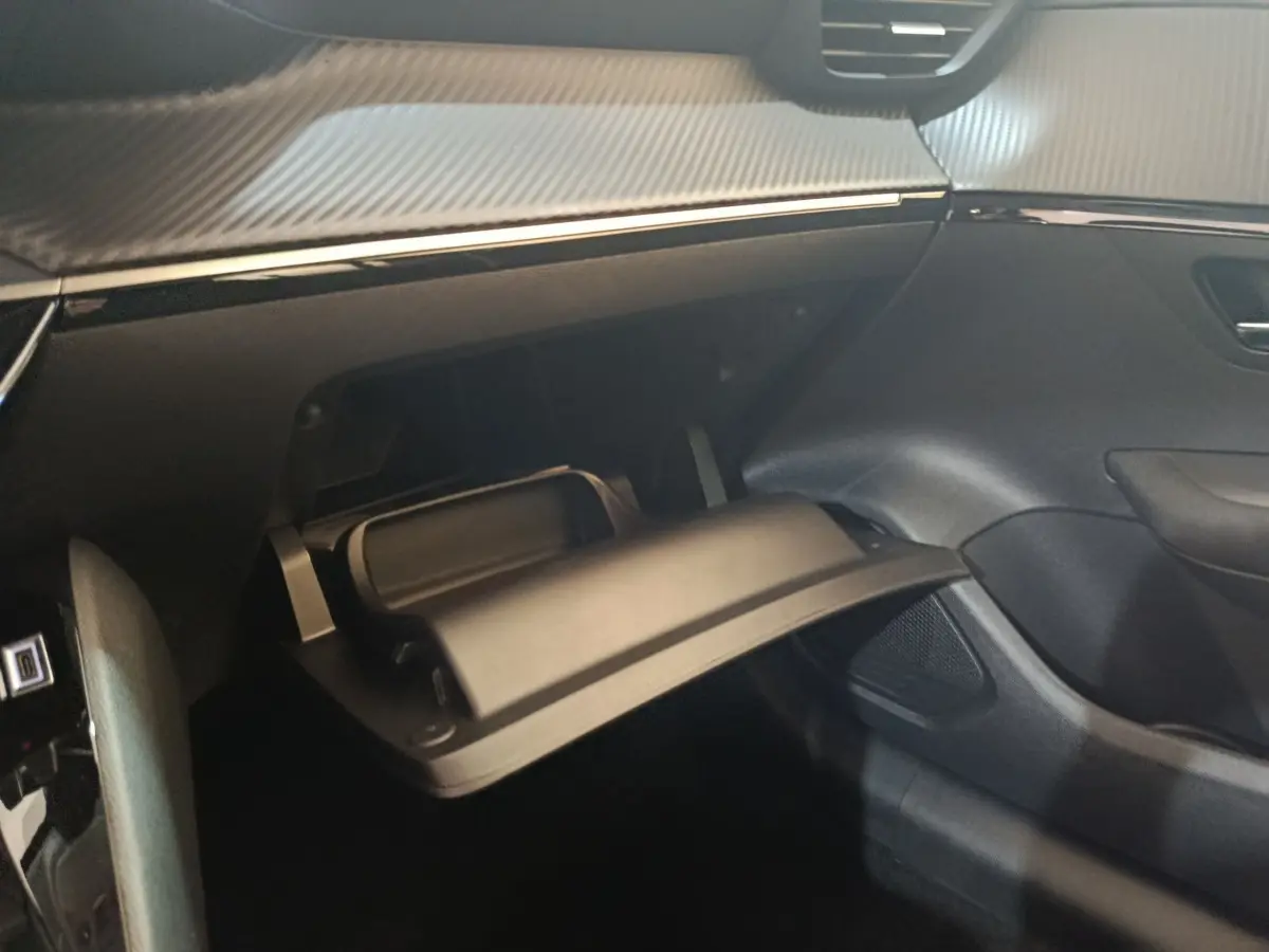 Intérieur de la Peugeot 208 électrique 2024, vue côté passager sur la boîte à gants ouverte avec finition noire et carbone.