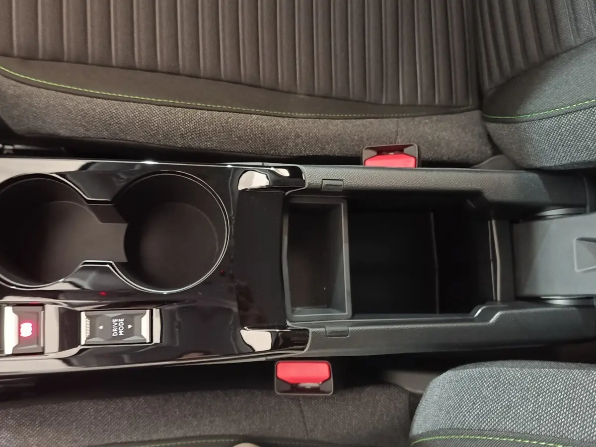 Vue plongeante sur la console centrale noire brillante de la Peugeot 208 électrique, avec porte-gobelets et rangement ouvert.