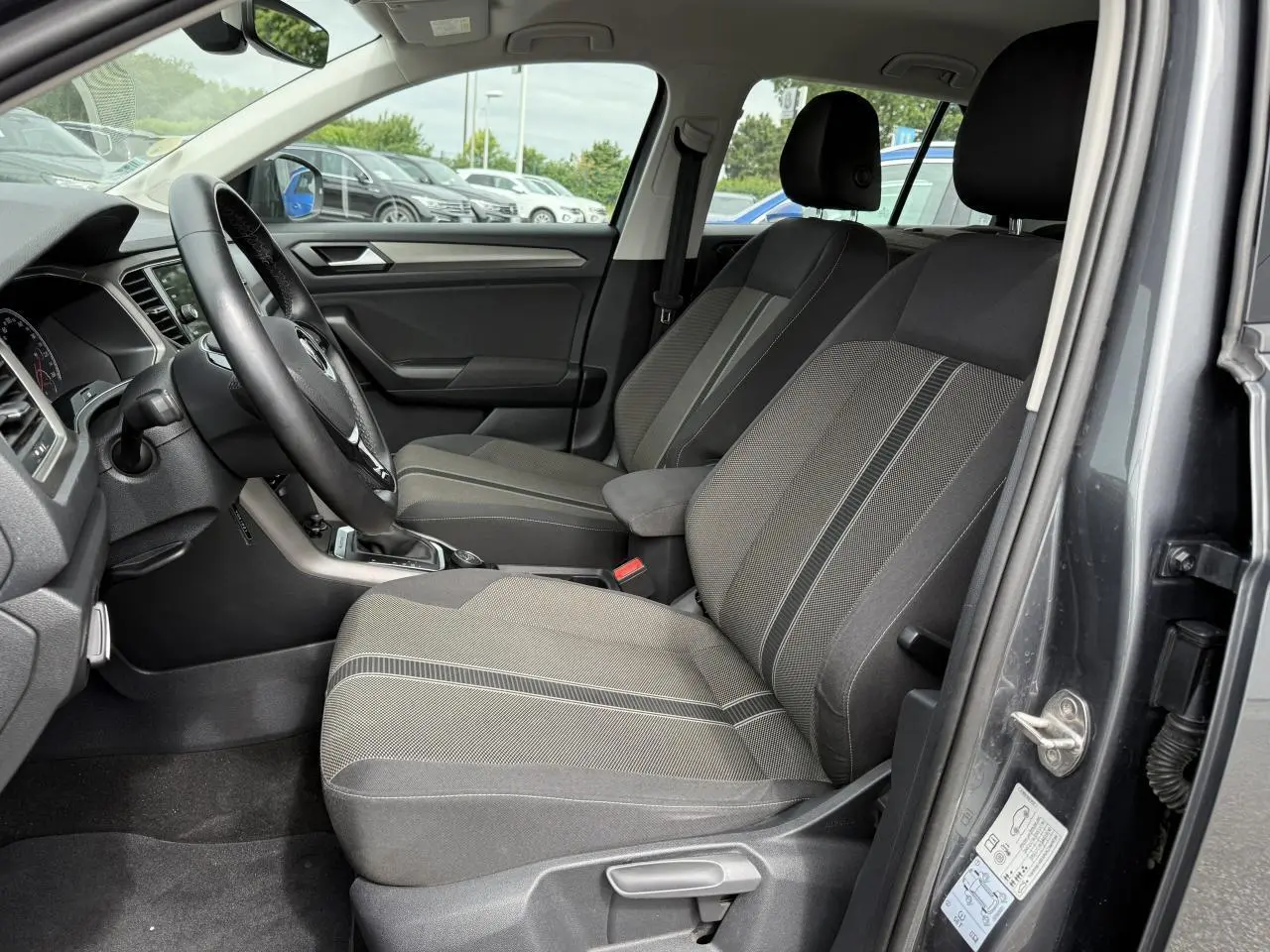 Vue intérieure côté conducteur du Volkswagen T-Roc gris Indium Metal, montrant les sièges avant et le volant multifonction en cuir.