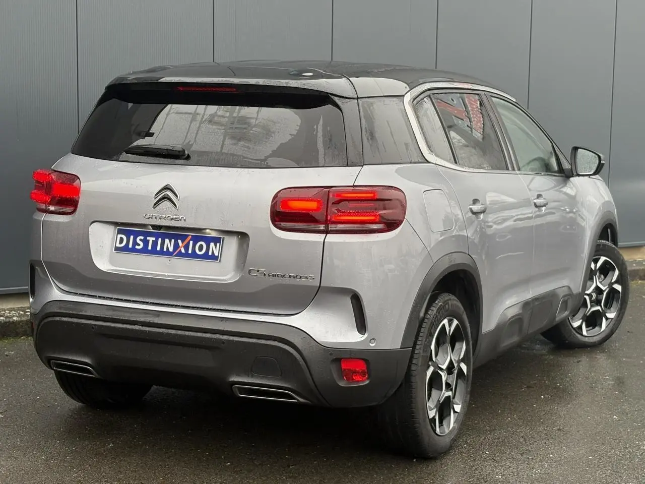 Vue 3/4 arrière droite d'un Citroën C5 Aircross Hybrid gris Artense avec toit noir et feux arrière LED allumés.