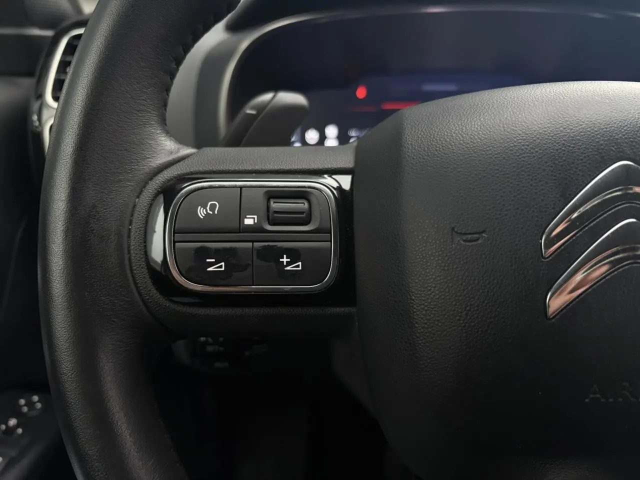 Gros plan sur le volant noir du Citroën C5 Aircross Hybrid 2024, avec commandes intégrées à gauche et logo chromé central.