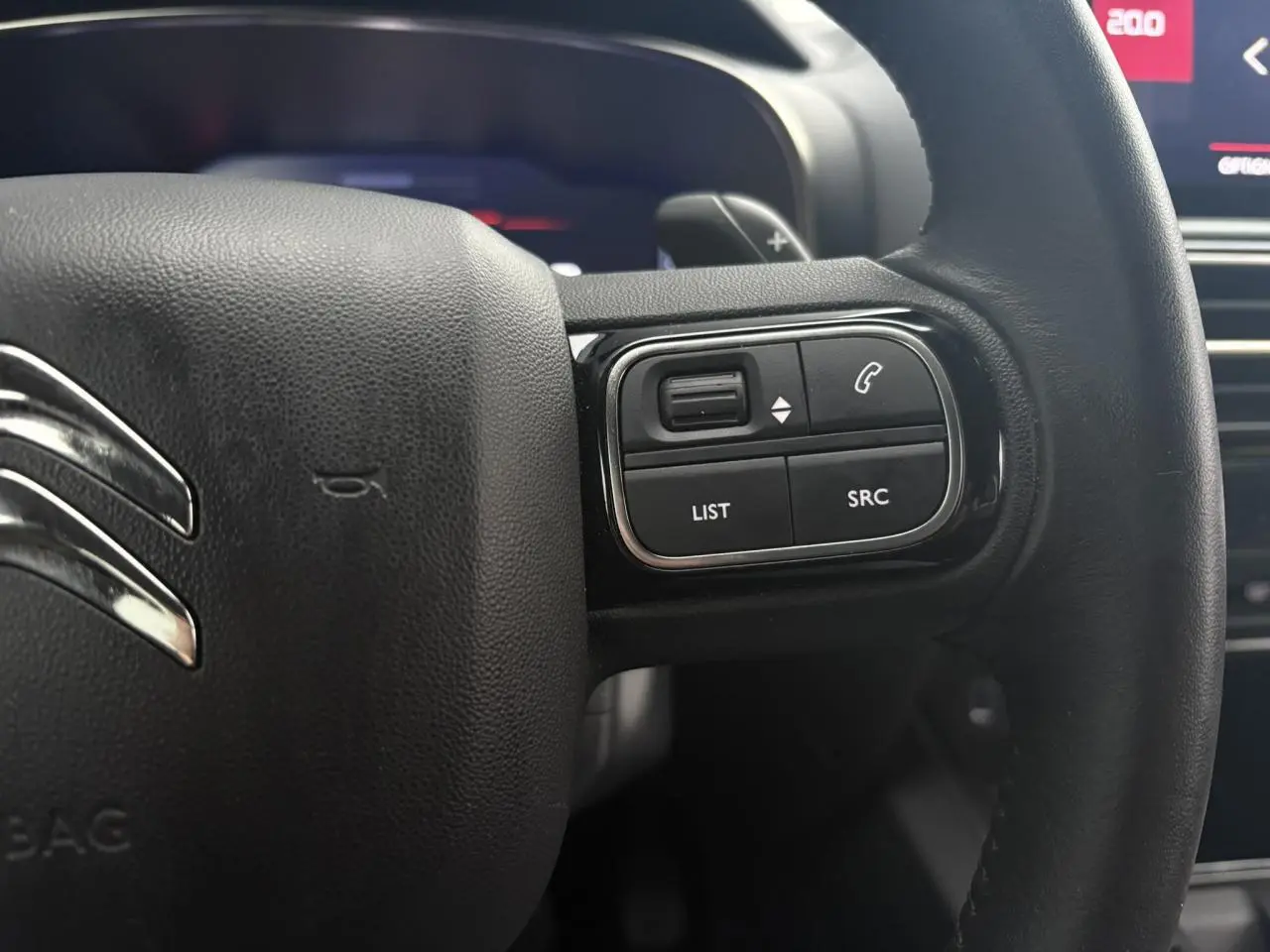 Gros plan sur le volant noir en cuir du Citroën C5 Aircross Hybrid 2024 avec commandes intégrées côté droit.