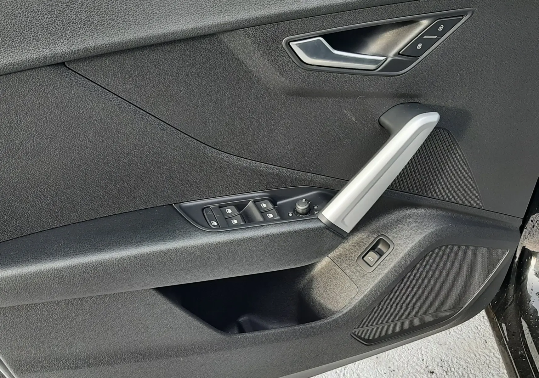 Gros plan sur la porte avant gauche noire de l'Audi Q2 35 TFSI S-Line avec commandes de vitres et poignée argentée.