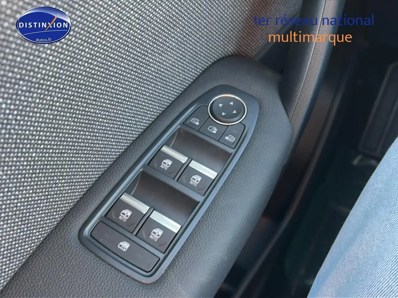 Gros plan sur les commandes des vitres électriques côté gauche, avec garniture textile grise et plastique noir.